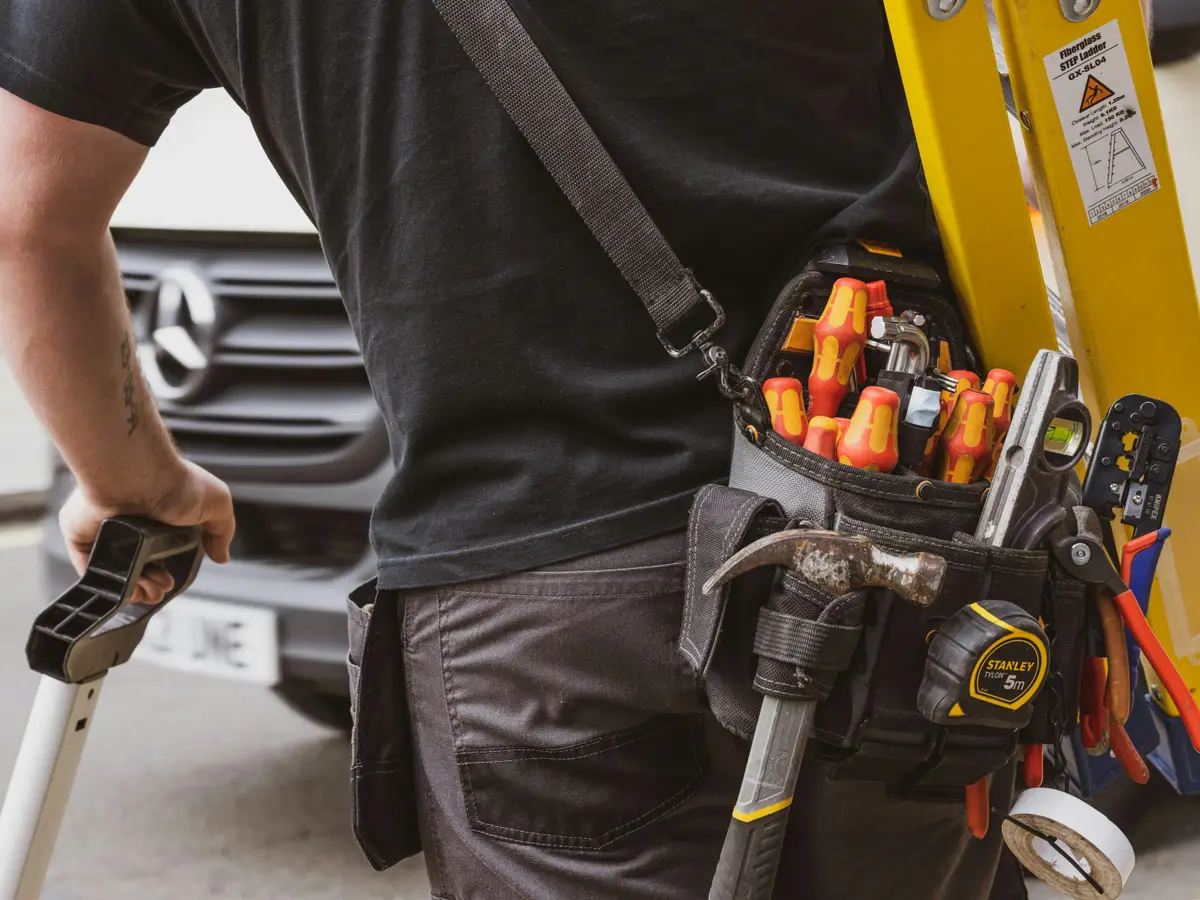 An electrician’s tool belt and ladder beside a work van